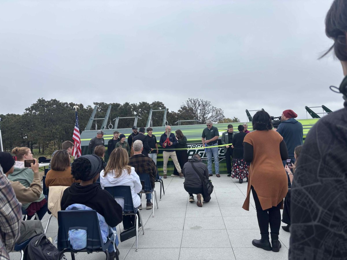A ribbon is stretched between several standing people as officials prepare to open the fitness court. Several people are seated in chairs and watching the ceremony.