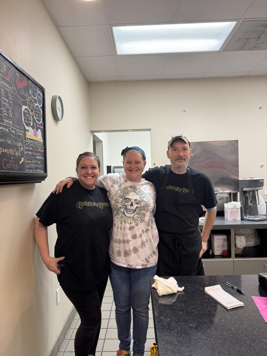 Three people stand together in front of a food counter.