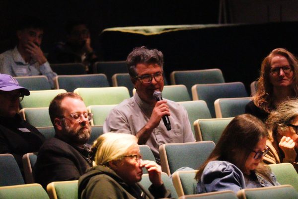 A man seated in an audience holds a microphone as he asks a question.