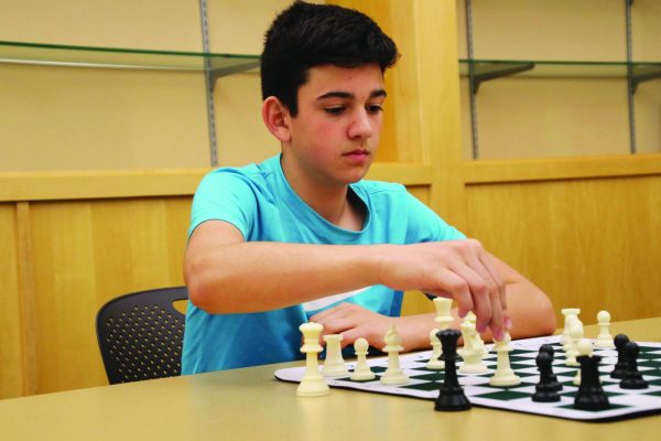 A teenager makes a move on a chess board while seated at a table.