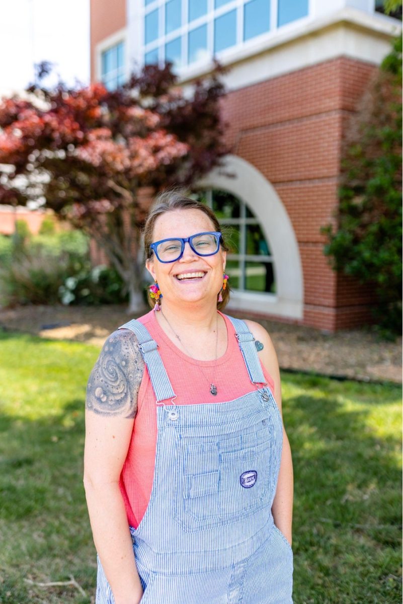 Woman wearing glasses and striped overalls stands in front of a building.