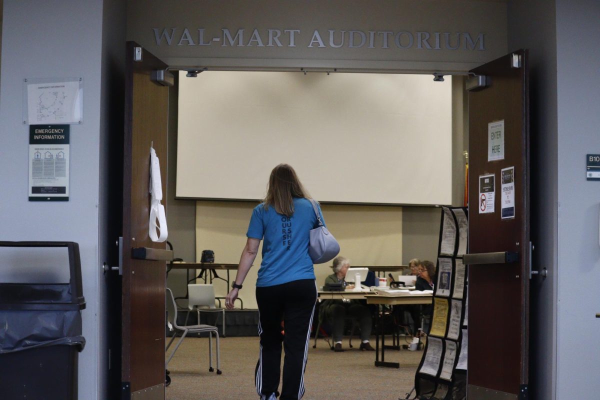 A woman, visible from the back, walks into a room with a sign above it reading "Walmart Auditorium."