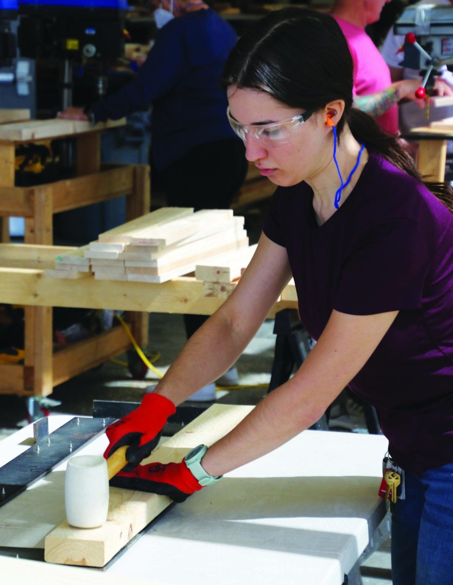 A volunteer wearing protective gloves and eyewear positions a board on a table.