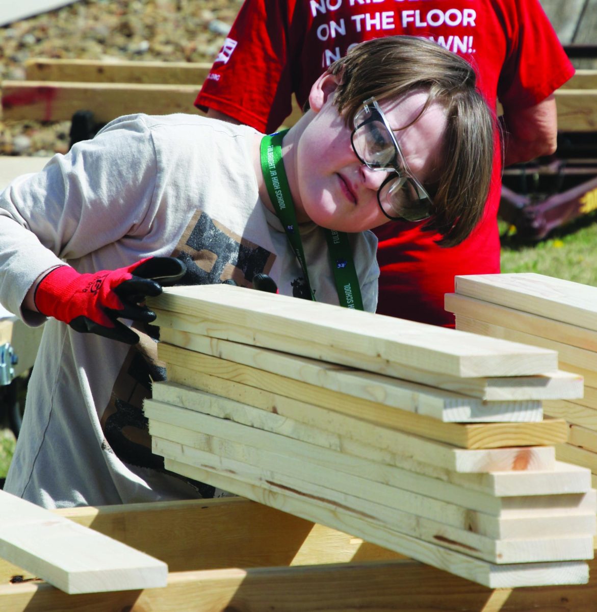 A female volunteer wearing protective eyewear moves a stack of boards.