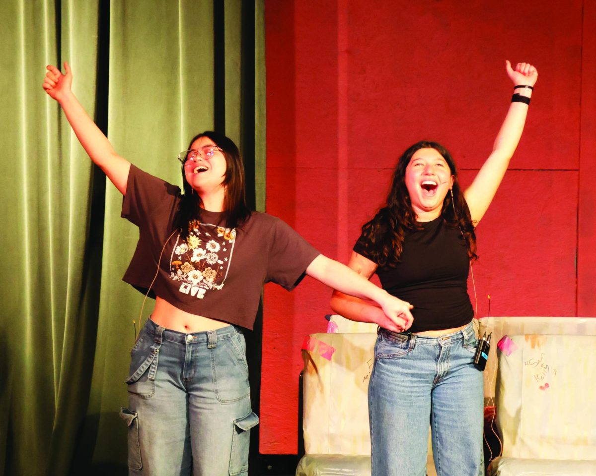 Two young actresses raise their right arms as they sing.