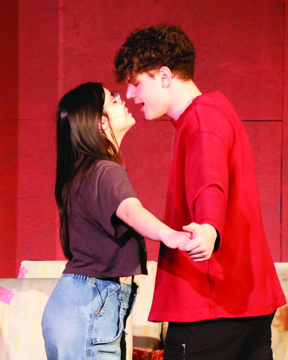 Two people, a girl (left), and a boy (right) rehearse a scene standing and facing each other.