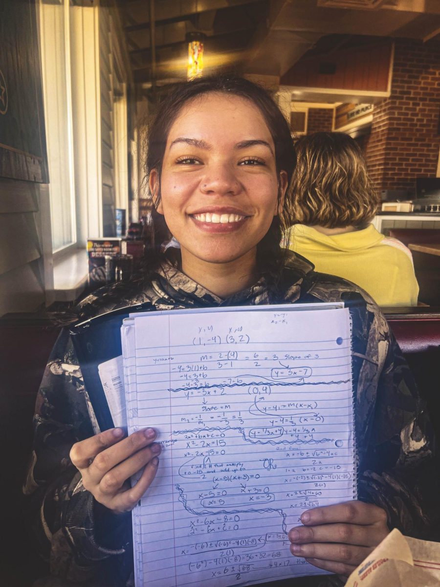 A student holds up a notebook that has math equations on it. The student is Charlzie Jones, the profile article subject.