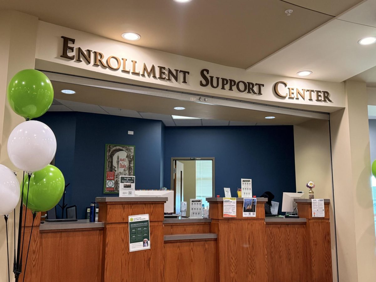 The photo shows a counter with fliers attached to the front facing customers. Above this area, the letters spell "Enrollment Support Center."