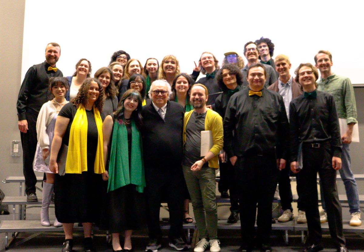 A group of people stands on risers that were used in a musical performance. The honored professor is at the center of the first row.