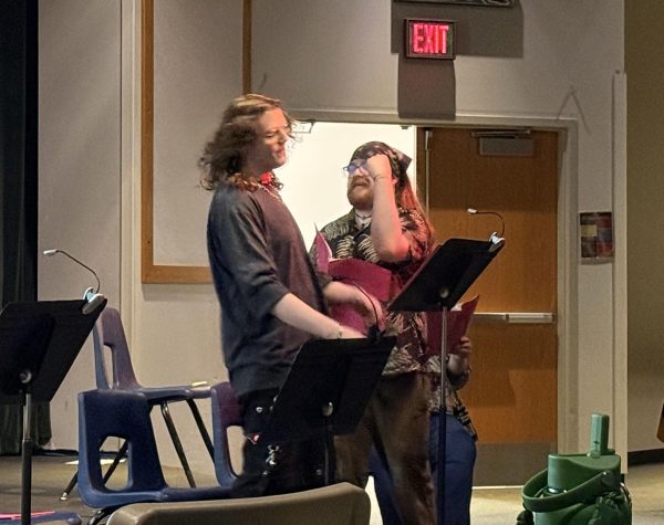 Two actors perform an excerpt during Playwrights in Process. The two are standing behind music stands, and the one on the right has his arm raised in front of his face.