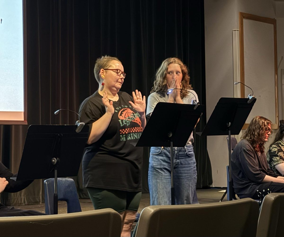 Two students act out their characters' parts during the April 15 Playwrights in Process. The two are standing behind music stands to deliver their lines.