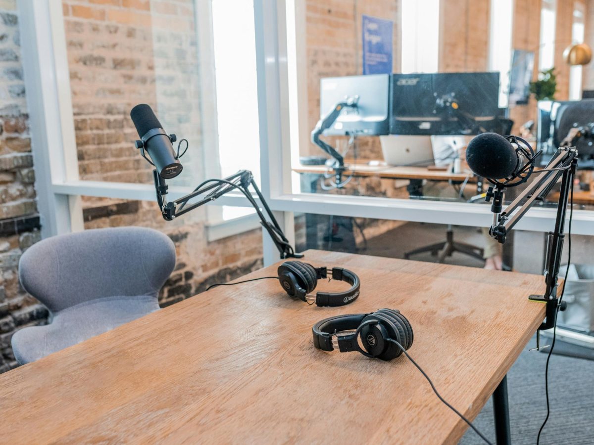 The photo shows an empty chair facing a table and two microphones for podcasting.