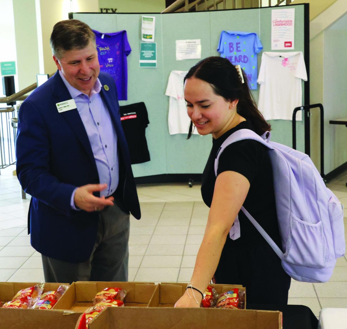 A man stands on the left and watches as a student reaches into a box of wrapped pastries.